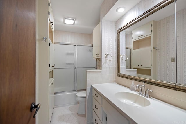 full bath featuring wallpapered walls, vanity, shower / bath combination with glass door, and toilet