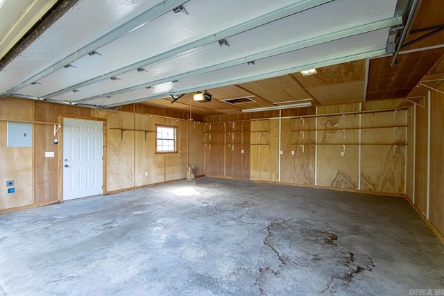 garage with electric panel, wood walls, and a garage door opener