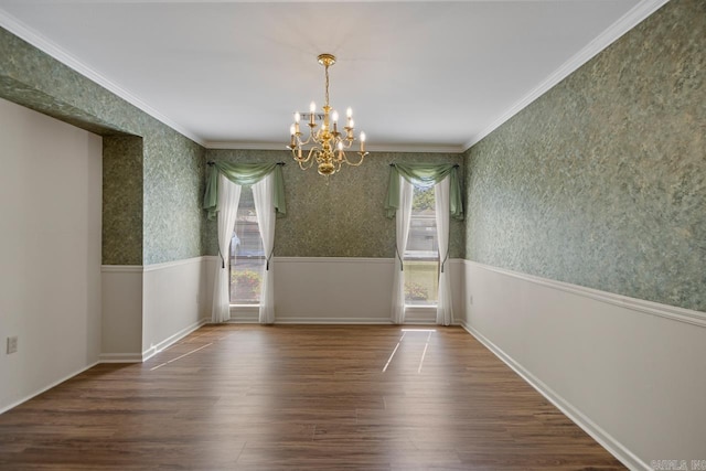 unfurnished dining area featuring baseboards, an inviting chandelier, wallpapered walls, wood finished floors, and crown molding