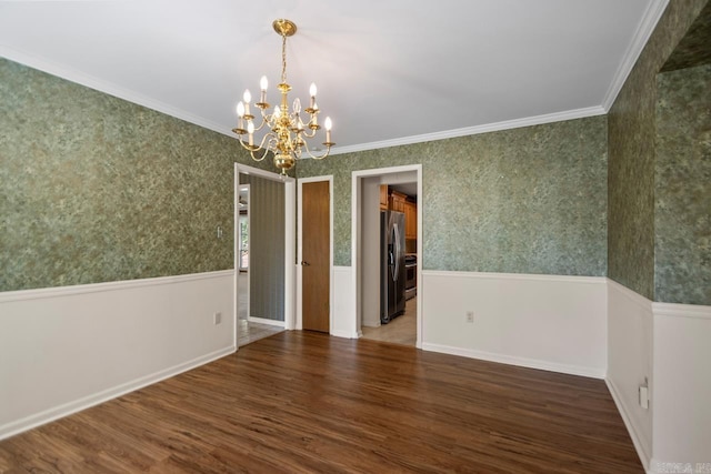 spare room featuring a wainscoted wall, a notable chandelier, wallpapered walls, wood finished floors, and crown molding