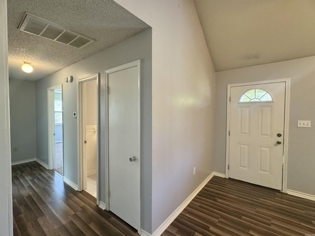 foyer entrance featuring vaulted ceiling, visible vents, dark wood-type flooring, baseboards, and a textured ceiling