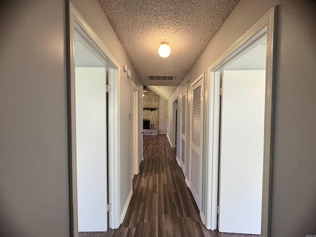 corridor with vaulted ceiling, visible vents, baseboards, a textured ceiling, and dark wood-style flooring