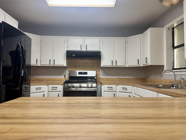 kitchen with stainless steel range with gas cooktop, a sink, freestanding refrigerator, under cabinet range hood, and wooden counters