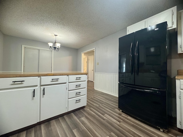 kitchen featuring dark wood finished floors, wainscoting, freestanding refrigerator, a notable chandelier, and white cabinetry