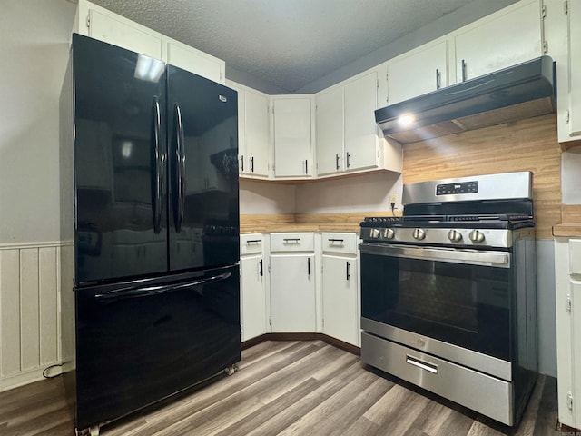 kitchen with wood finished floors, under cabinet range hood, stainless steel range with gas stovetop, and freestanding refrigerator