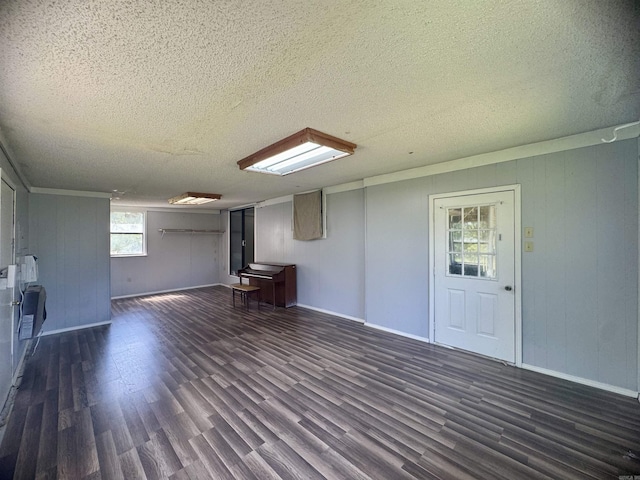 interior space featuring wooden walls, baseboards, a textured ceiling, and dark wood-style flooring