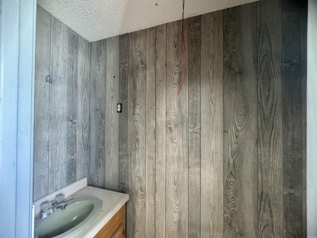 bathroom featuring a textured ceiling, wood walls, and vanity
