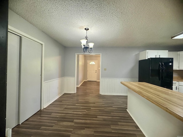 corridor featuring wainscoting, a textured ceiling, a chandelier, and dark wood finished floors
