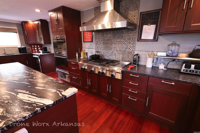 kitchen featuring wall chimney range hood, appliances with stainless steel finishes, dark wood-style flooring, and a sink