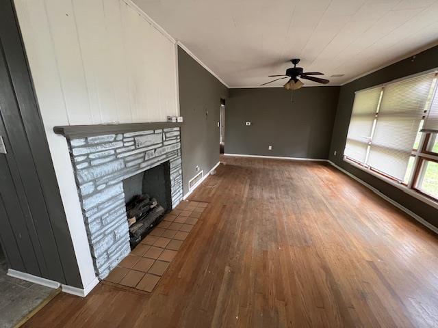 unfurnished living room with ceiling fan, ornamental molding, wood finished floors, and a fireplace