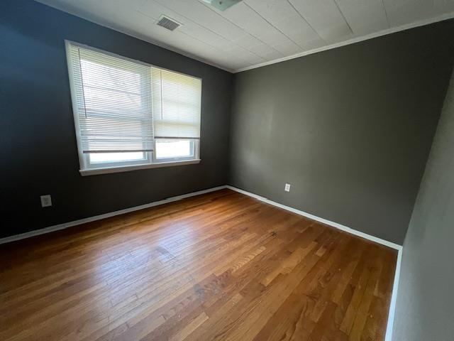 unfurnished room featuring visible vents, baseboards, wood finished floors, and crown molding