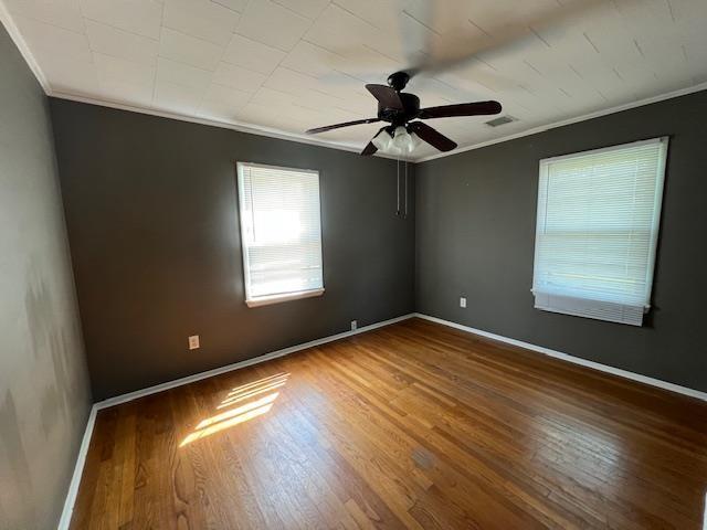 unfurnished room with wood finished floors, visible vents, a ceiling fan, crown molding, and baseboards