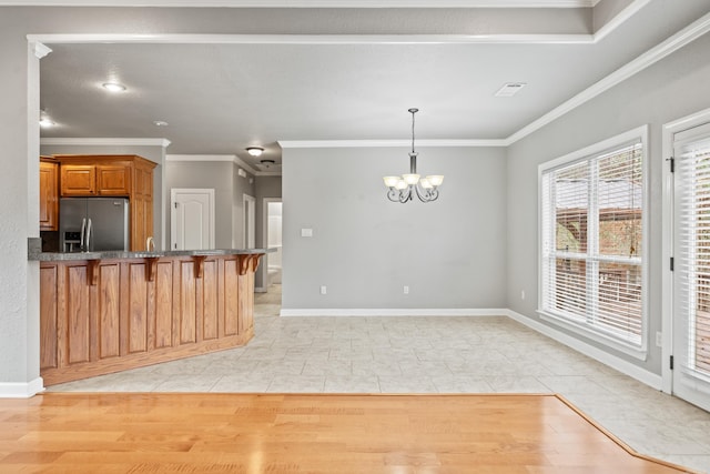 kitchen with stainless steel fridge with ice dispenser, ornamental molding, a chandelier, a kitchen bar, and brown cabinetry
