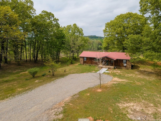 chalet / cabin with a forest view, gravel driveway, a front yard, and metal roof