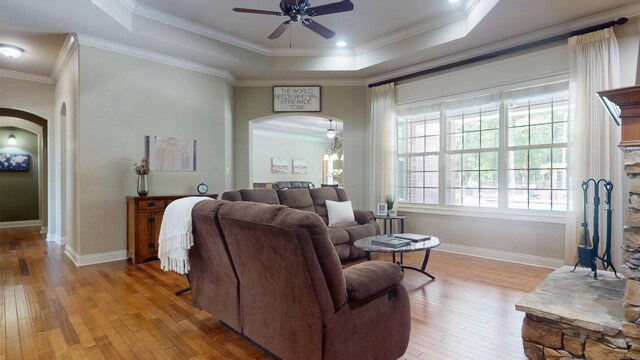 living area with light wood-style floors, ceiling fan, arched walkways, a tray ceiling, and baseboards