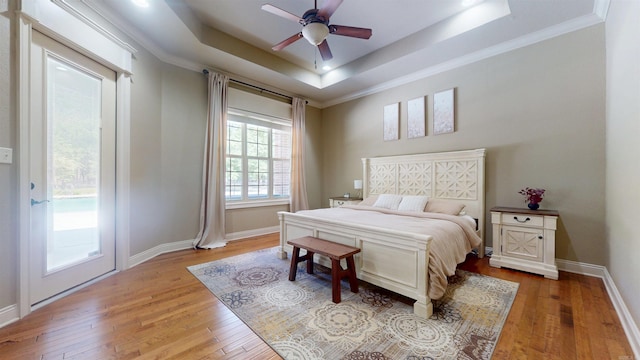 bedroom with light wood finished floors, baseboards, a raised ceiling, and access to exterior