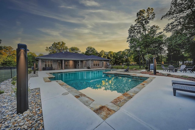 pool at dusk featuring an outdoor pool, a patio, and fence