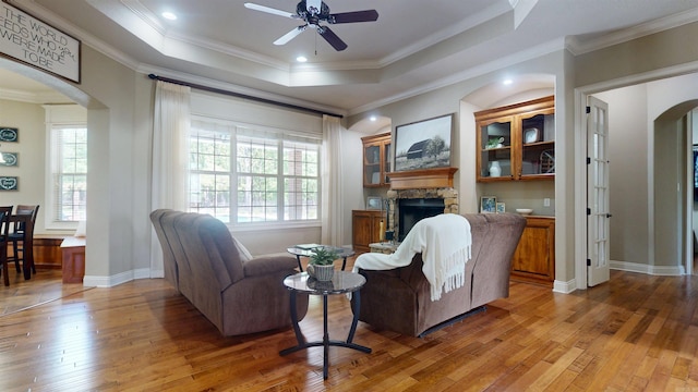living room with light wood-type flooring, plenty of natural light, a ceiling fan, and arched walkways