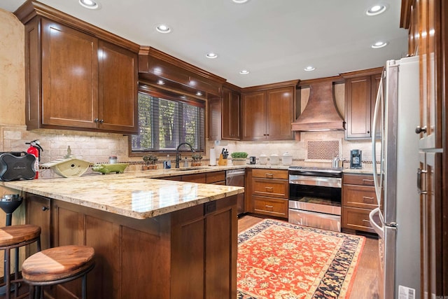 kitchen featuring light wood finished floors, stainless steel appliances, a peninsula, custom range hood, and light stone countertops