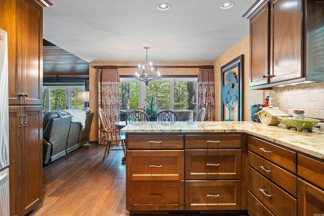 kitchen with a chandelier, dark wood finished floors, backsplash, light stone countertops, and a peninsula