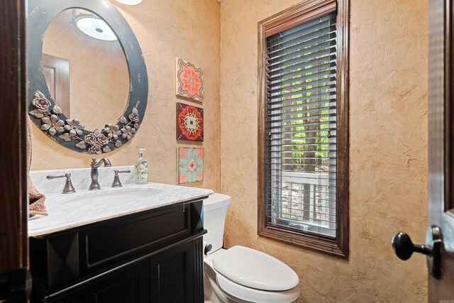 bathroom featuring toilet, a textured wall, and vanity