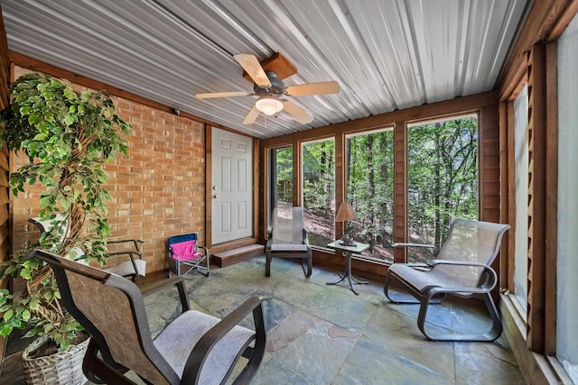 sunroom / solarium featuring brick wall, stone tile flooring, and ceiling fan