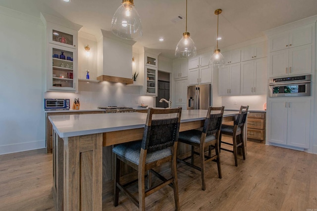 4941 Lake Vista Dr, Benton, AR 72019 - kitchen with stainless steel appliances, a kitchen island with sink, light wood-type flooring, visible vents, and premium range hood