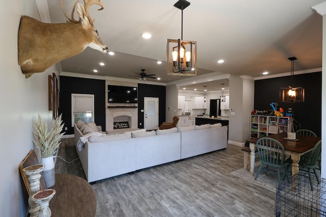 living area with recessed lighting, wood finished floors, ornamental molding, a fireplace, and ceiling fan with notable chandelier