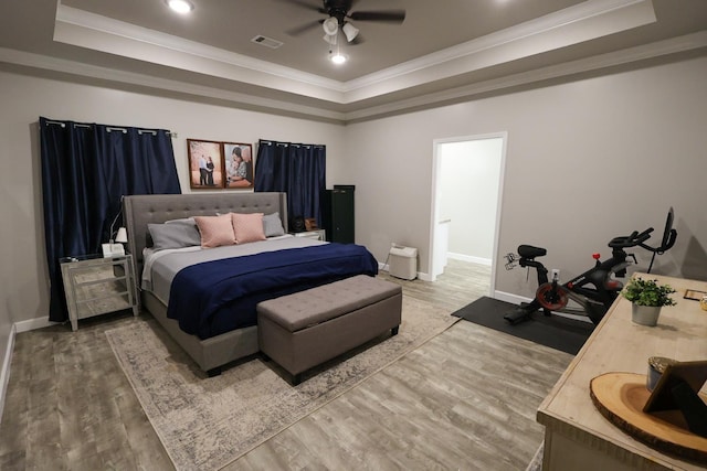 bedroom with a tray ceiling, visible vents, light wood-style floors, crown molding, and baseboards