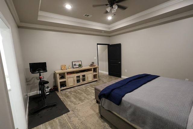 bedroom with a raised ceiling, visible vents, crown molding, baseboards, and light wood-style flooring