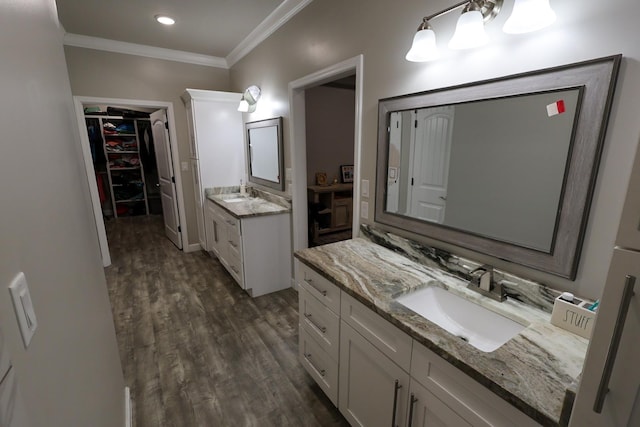 bathroom with crown molding, wood finished floors, a sink, a walk in closet, and two vanities