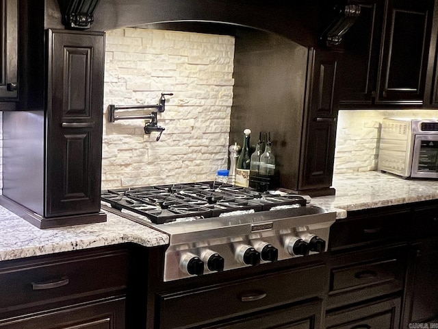 2780 Shoemaker Rd, Sheridan, AR 72150 - kitchen featuring a toaster, backsplash, stainless steel gas stovetop, dark cabinetry, and light stone countertops