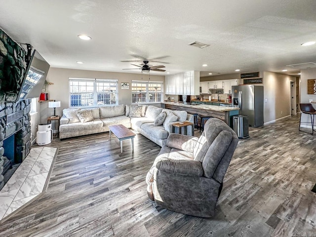 living room with a stone fireplace, wood finished floors, a textured ceiling, and ceiling fan