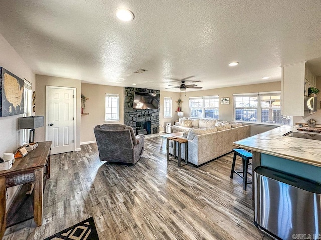 living area featuring dark wood-type flooring, a textured ceiling, a healthy amount of sunlight, and a fireplace