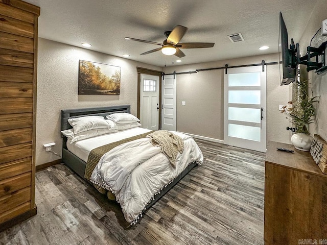 bedroom featuring a textured ceiling, a barn door, visible vents, recessed lighting, and wood finished floors