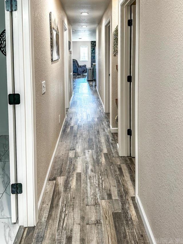 hall featuring baseboards, a textured wall, and dark wood-style floors