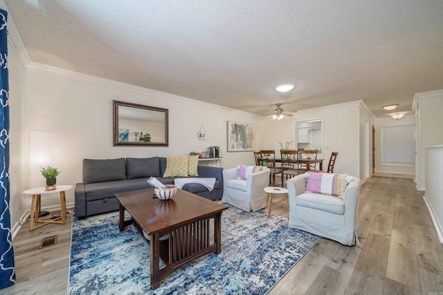 living room with crown molding, a textured ceiling, ceiling fan, light wood-style flooring, and visible vents