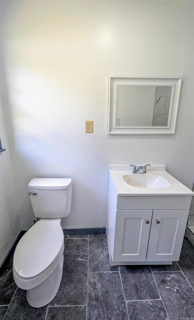 half bath with baseboards, vanity, and toilet