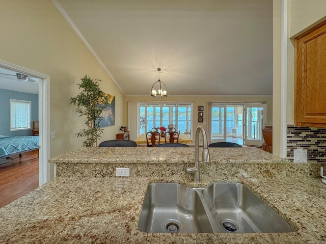 kitchen featuring light stone counters, ornamental molding, a sink, and a healthy amount of sunlight