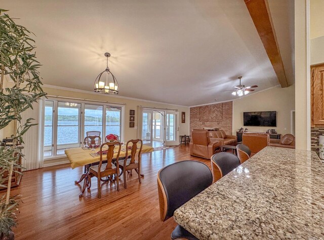dining space with ceiling fan with notable chandelier, vaulted ceiling with beams, light wood-type flooring, a fireplace, and ornamental molding