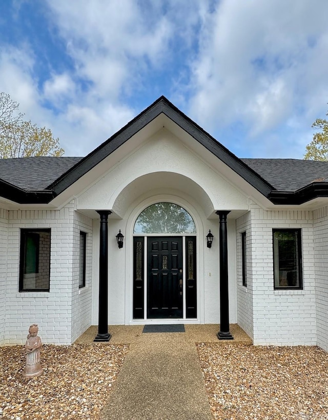 doorway to property with brick siding and a shingled roof