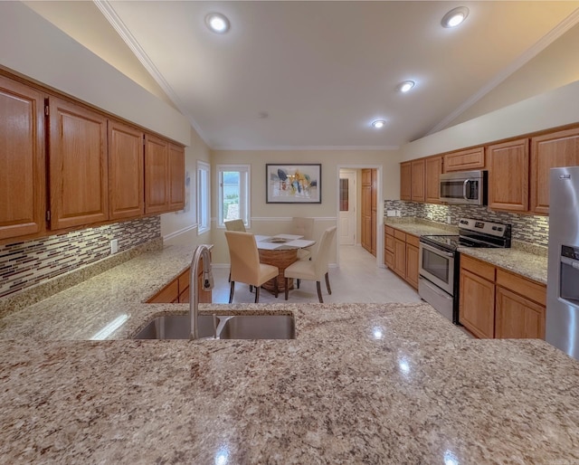 kitchen with lofted ceiling, light stone counters, stainless steel appliances, and a sink