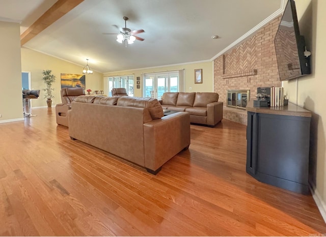living room with a ceiling fan, crown molding, lofted ceiling with beams, light wood-style flooring, and a brick fireplace
