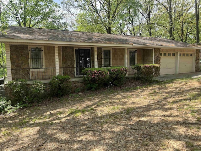ranch-style home featuring a porch, driveway, stone siding, and a garage