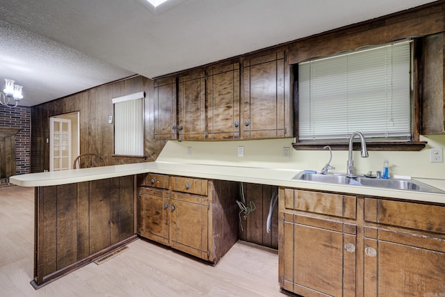 kitchen featuring visible vents, a peninsula, light wood-style floors, light countertops, and a sink