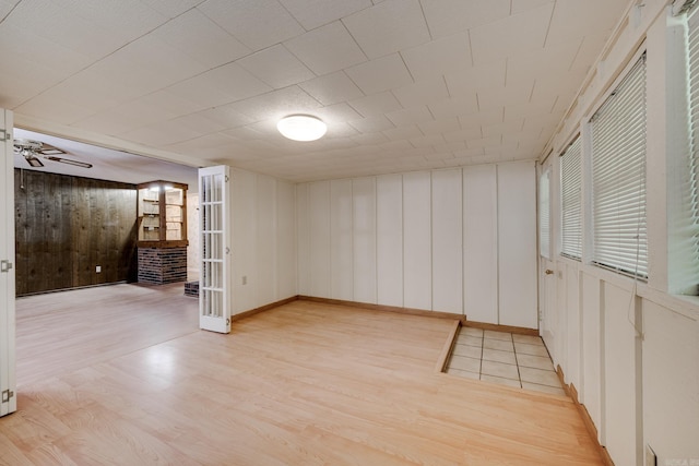 basement with a decorative wall, baseboards, wood walls, and light wood-style floors