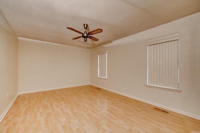 empty room with ceiling fan, a textured ceiling, baseboards, wood finished floors, and visible vents