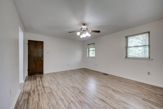 empty room featuring ceiling fan, a textured ceiling, visible vents, baseboards, and light wood-style flooring