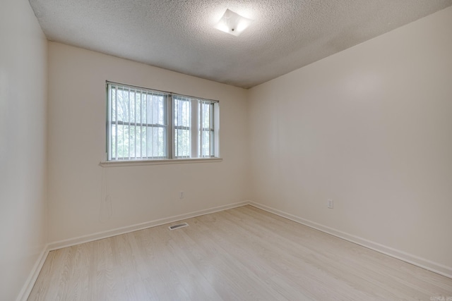 spare room featuring visible vents, baseboards, a textured ceiling, and wood finished floors
