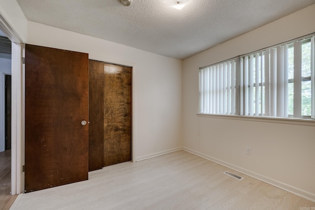 unfurnished bedroom featuring baseboards, a textured ceiling, visible vents, and wood finished floors